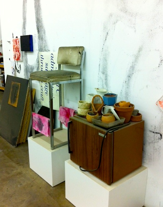 Inside the studio of Amanda Ross-Ho, where a chair and an assortment of containers sit atop pedestals